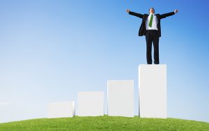 Business Man Outdoors Standing on a Bar Graph with Arms Raised